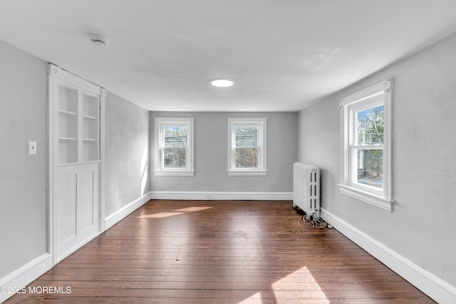 spare room featuring plenty of natural light, radiator heating unit, baseboards, and hardwood / wood-style floors