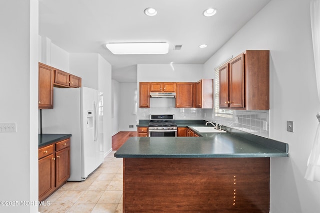 kitchen with stainless steel range, under cabinet range hood, a sink, dark countertops, and white fridge with ice dispenser