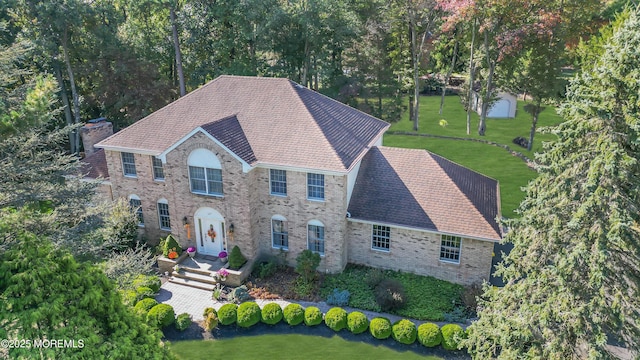 colonial-style house with a front yard, brick siding, and roof with shingles