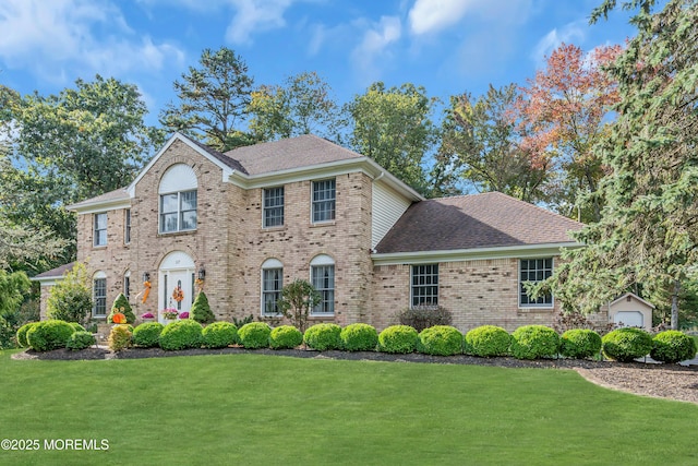 view of front facade with brick siding, a shingled roof, and a front yard