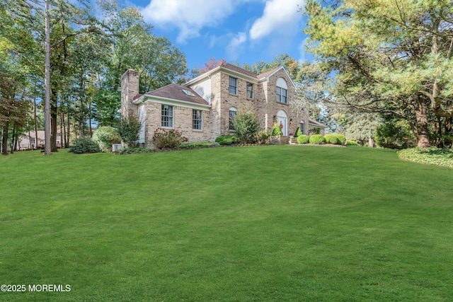 view of front facade featuring brick siding, a chimney, and a front lawn