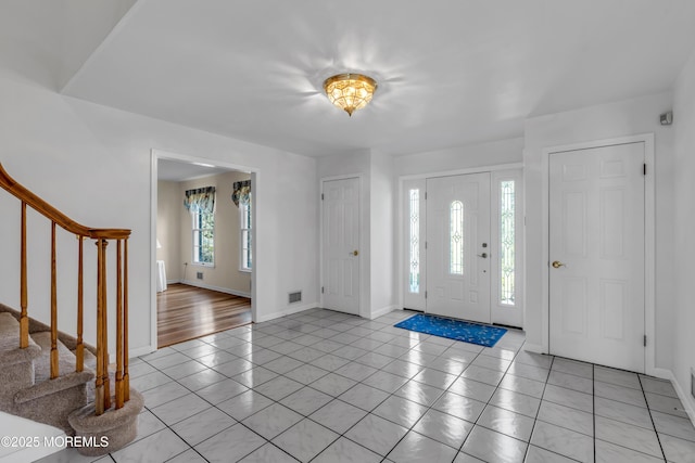 foyer entrance with light tile patterned floors, visible vents, stairs, and baseboards