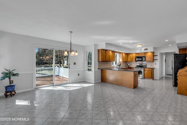 kitchen featuring brown cabinetry, a peninsula, stainless steel appliances, a notable chandelier, and tasteful backsplash