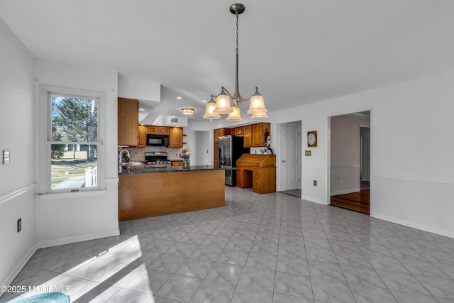 kitchen featuring backsplash, dark countertops, appliances with stainless steel finishes, a peninsula, and brown cabinetry