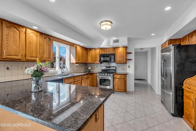 kitchen featuring brown cabinets, a sink, dark stone counters, appliances with stainless steel finishes, and a peninsula