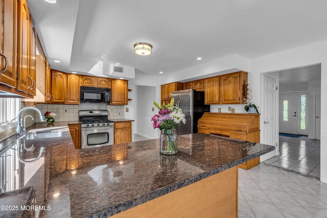 kitchen featuring backsplash, appliances with stainless steel finishes, a peninsula, light tile patterned flooring, and a sink