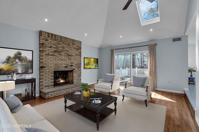 living area with visible vents, high vaulted ceiling, a brick fireplace, and wood finished floors