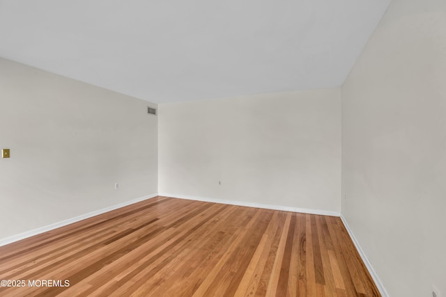 empty room with hardwood / wood-style floors, visible vents, and baseboards