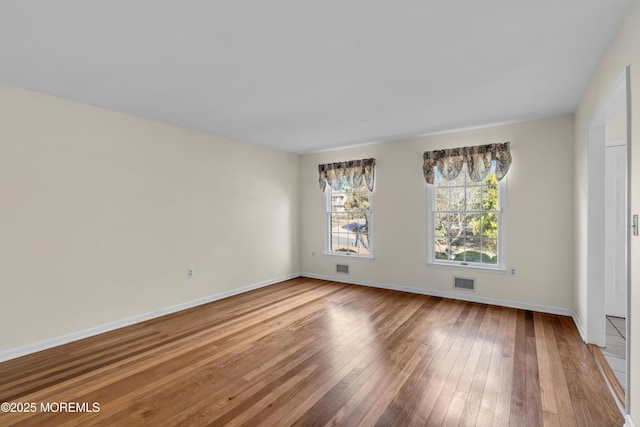 empty room featuring visible vents, wood-type flooring, and baseboards