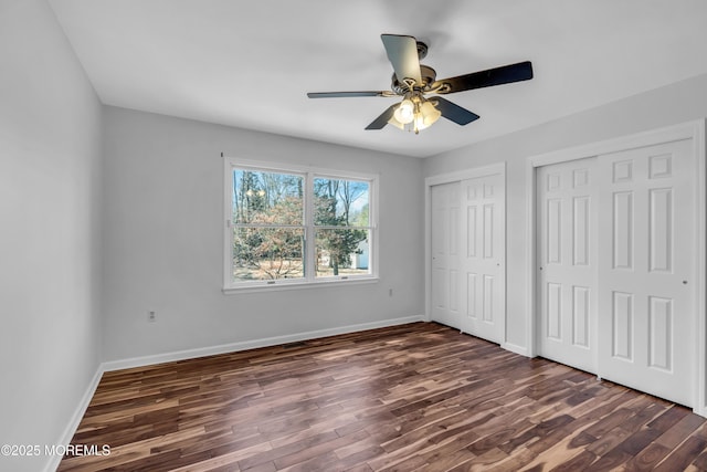 unfurnished bedroom featuring dark wood-style floors, baseboards, two closets, and ceiling fan