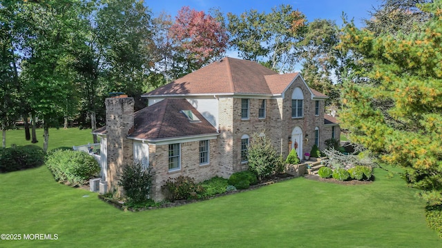 colonial house featuring brick siding, cooling unit, a chimney, and a front yard