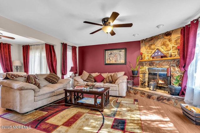 living room featuring wood finished floors, a stone fireplace, and ceiling fan