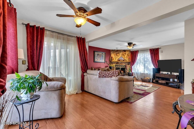 living area featuring a stone fireplace, wood finished floors, and a ceiling fan