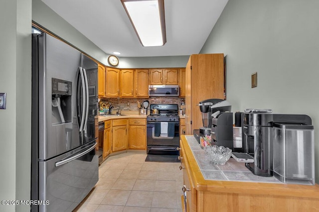 kitchen with tasteful backsplash, tile countertops, light tile patterned flooring, black appliances, and a sink