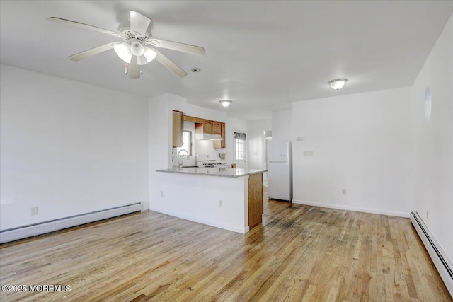 kitchen featuring light wood finished floors, a baseboard radiator, a peninsula, freestanding refrigerator, and a baseboard heating unit