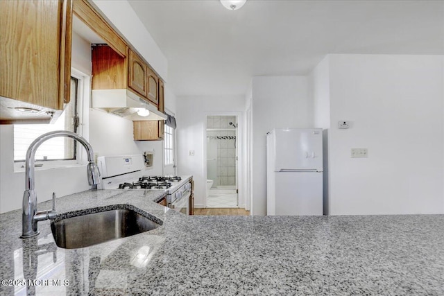 kitchen with a sink, white appliances, light stone counters, and a wealth of natural light