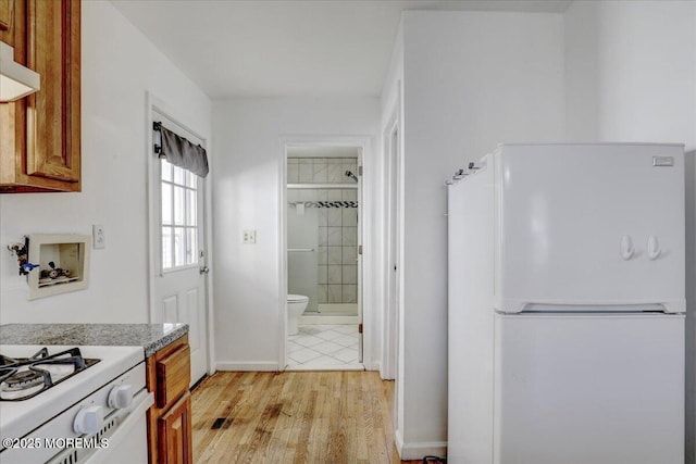 kitchen featuring light wood finished floors, baseboards, under cabinet range hood, brown cabinets, and white appliances