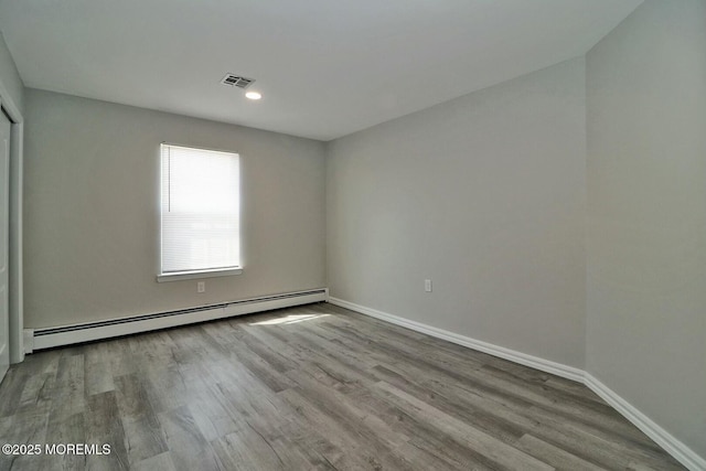 spare room featuring a baseboard radiator, baseboards, visible vents, and wood finished floors