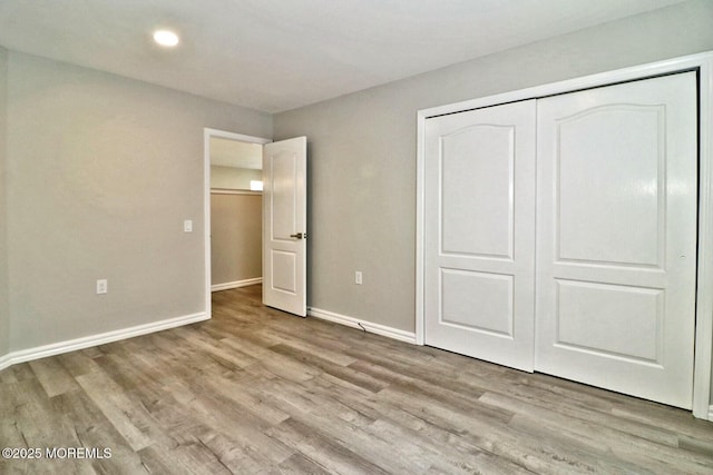 unfurnished bedroom with a closet, recessed lighting, light wood-style flooring, and baseboards