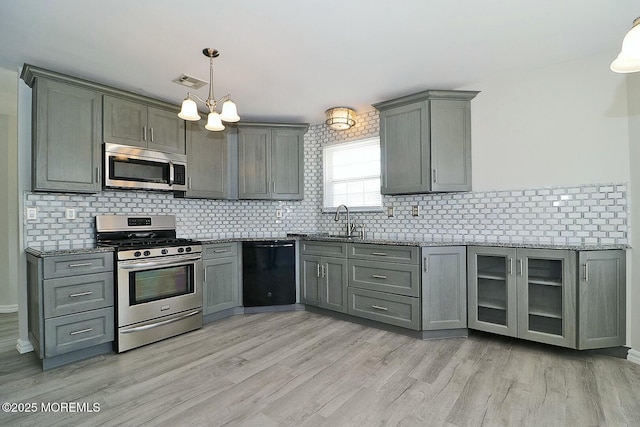 kitchen featuring visible vents, gray cabinetry, dark stone countertops, stainless steel appliances, and light wood finished floors