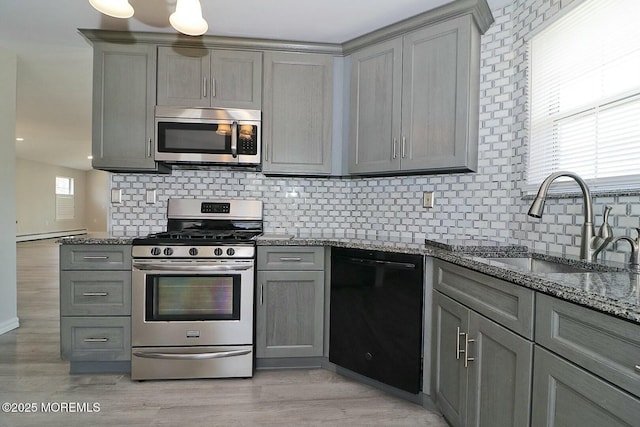 kitchen with light wood finished floors, gray cabinetry, stone counters, stainless steel appliances, and a sink