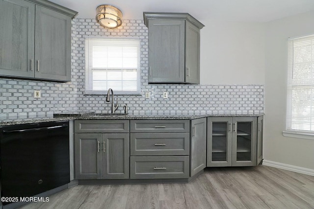 kitchen with backsplash, gray cabinetry, black dishwasher, stone countertops, and a sink