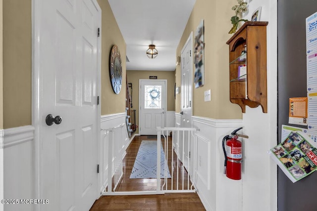 doorway with a decorative wall, wainscoting, and wood finished floors