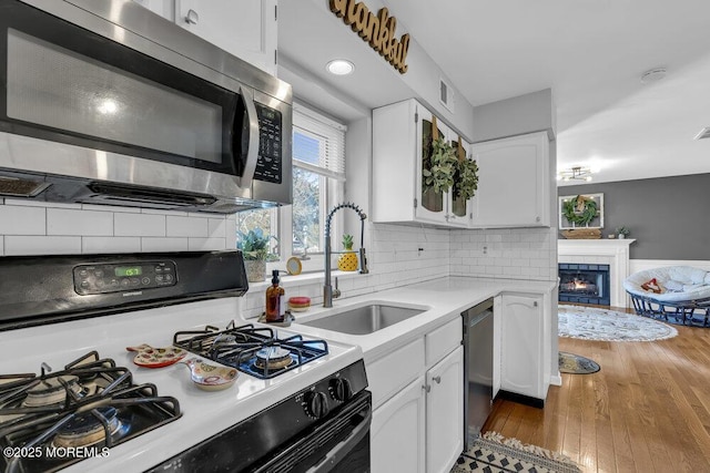 kitchen featuring a sink, hardwood / wood-style floors, appliances with stainless steel finishes, white cabinets, and a tile fireplace