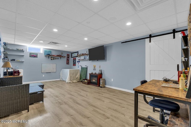 office area featuring a drop ceiling, baseboards, light wood-type flooring, and a barn door