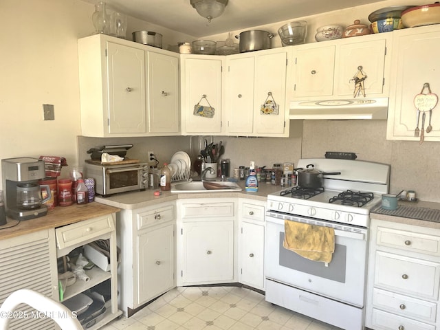 kitchen with a sink, light countertops, under cabinet range hood, white cabinetry, and white gas range