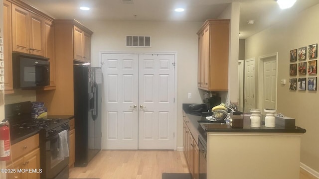 kitchen with visible vents, light wood finished floors, a sink, black appliances, and dark countertops