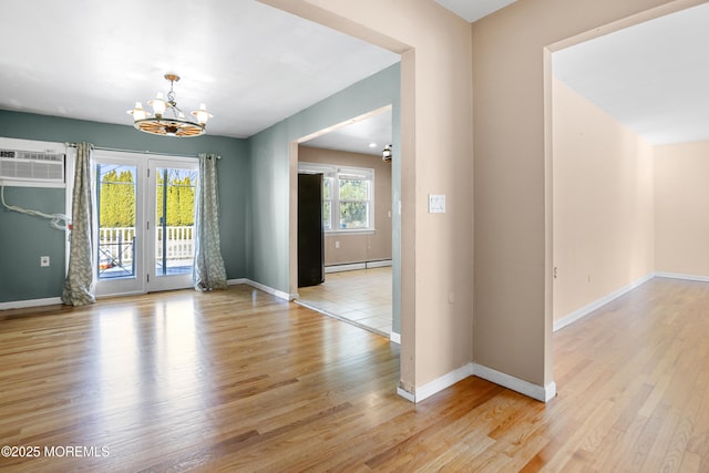 empty room with a wall unit AC, a notable chandelier, light wood-type flooring, and a baseboard radiator