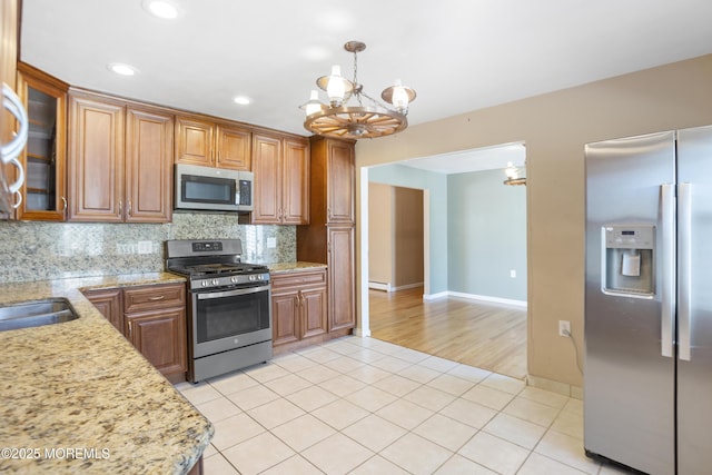 kitchen with brown cabinets, tasteful backsplash, appliances with stainless steel finishes, light tile patterned floors, and a chandelier