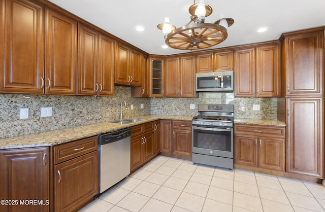 kitchen featuring glass insert cabinets, light tile patterned floors, decorative backsplash, stainless steel appliances, and a sink