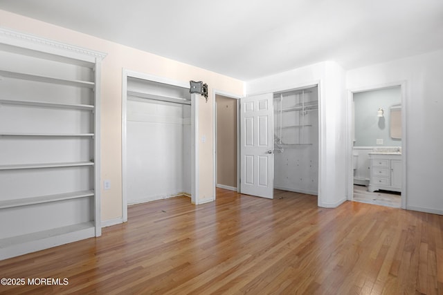 unfurnished bedroom featuring multiple closets, light wood-style flooring, ensuite bathroom, a barn door, and baseboards