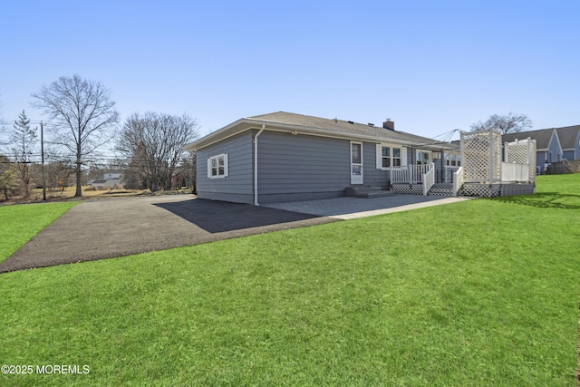 rear view of house featuring a patio area, driveway, a wooden deck, and a yard