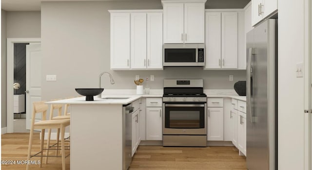 kitchen featuring light wood-type flooring, a sink, white cabinetry, stainless steel appliances, and a peninsula