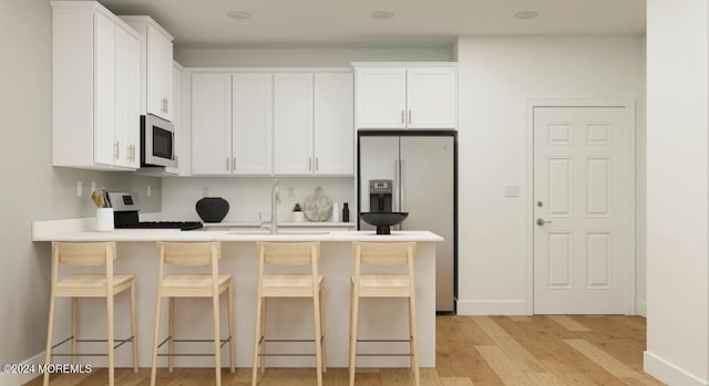 kitchen with a peninsula, a sink, appliances with stainless steel finishes, white cabinetry, and a kitchen breakfast bar