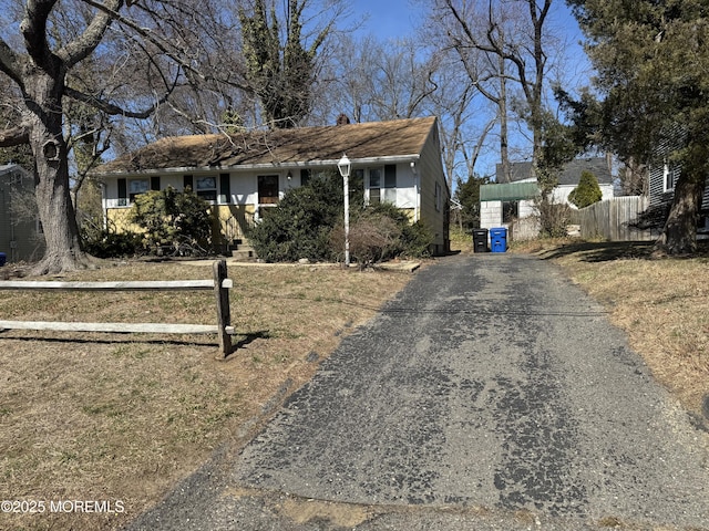 view of front of home with driveway, a chimney, and fence