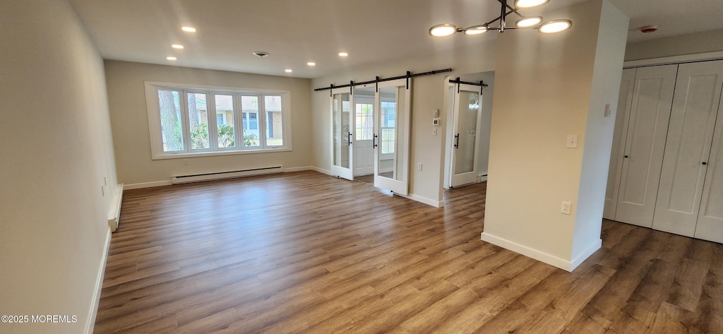 interior space featuring baseboards, a barn door, baseboard heating, recessed lighting, and wood finished floors