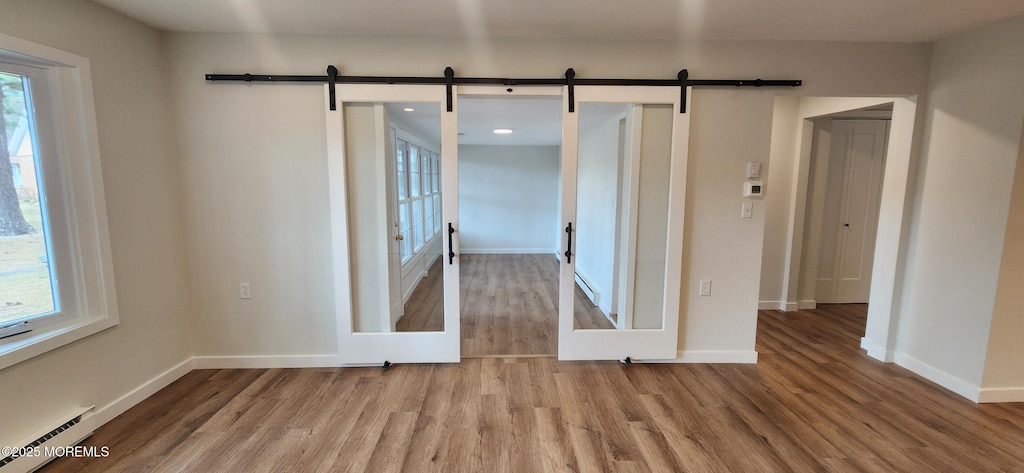 spare room with a barn door, wood finished floors, baseboards, and baseboard heating