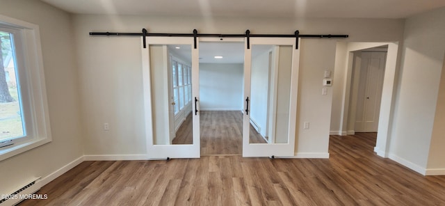 spare room with a barn door, wood finished floors, baseboards, and baseboard heating