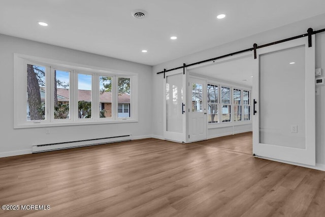 interior space featuring a baseboard heating unit, a barn door, light wood-style floors, and visible vents