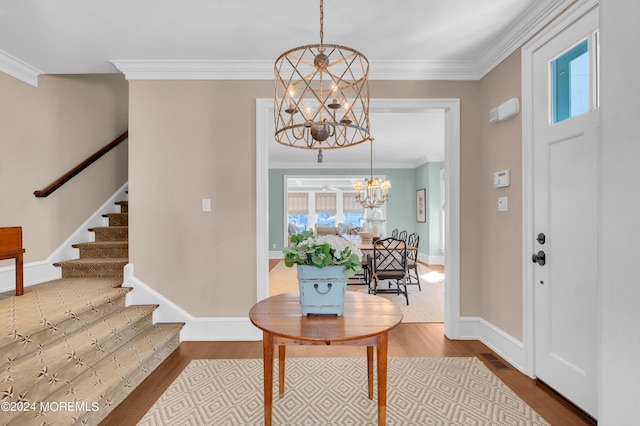 foyer entrance with stairs, ornamental molding, wood finished floors, and a chandelier