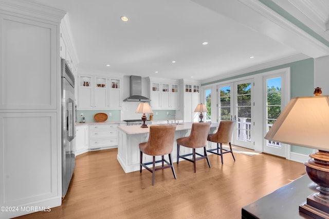 kitchen featuring light wood-style flooring, wall chimney range hood, white cabinetry, crown molding, and light countertops