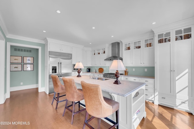 kitchen with visible vents, a sink, built in fridge, white cabinetry, and wall chimney range hood