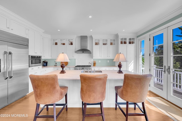 kitchen featuring stainless steel appliances, light countertops, french doors, white cabinetry, and wall chimney exhaust hood