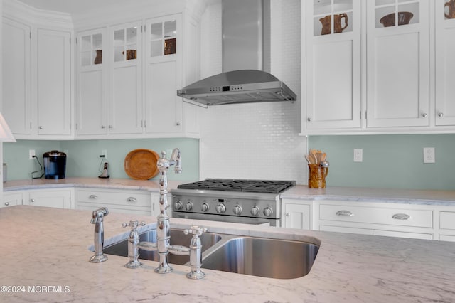 kitchen with glass insert cabinets, light stone countertops, white cabinets, and wall chimney range hood