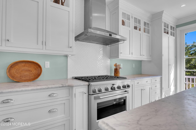 kitchen with tasteful backsplash, white cabinets, high end range, and wall chimney range hood