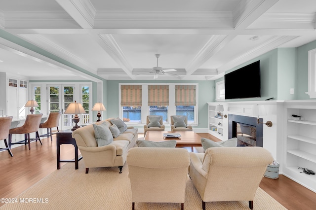 living area with a glass covered fireplace, crown molding, wood finished floors, and coffered ceiling